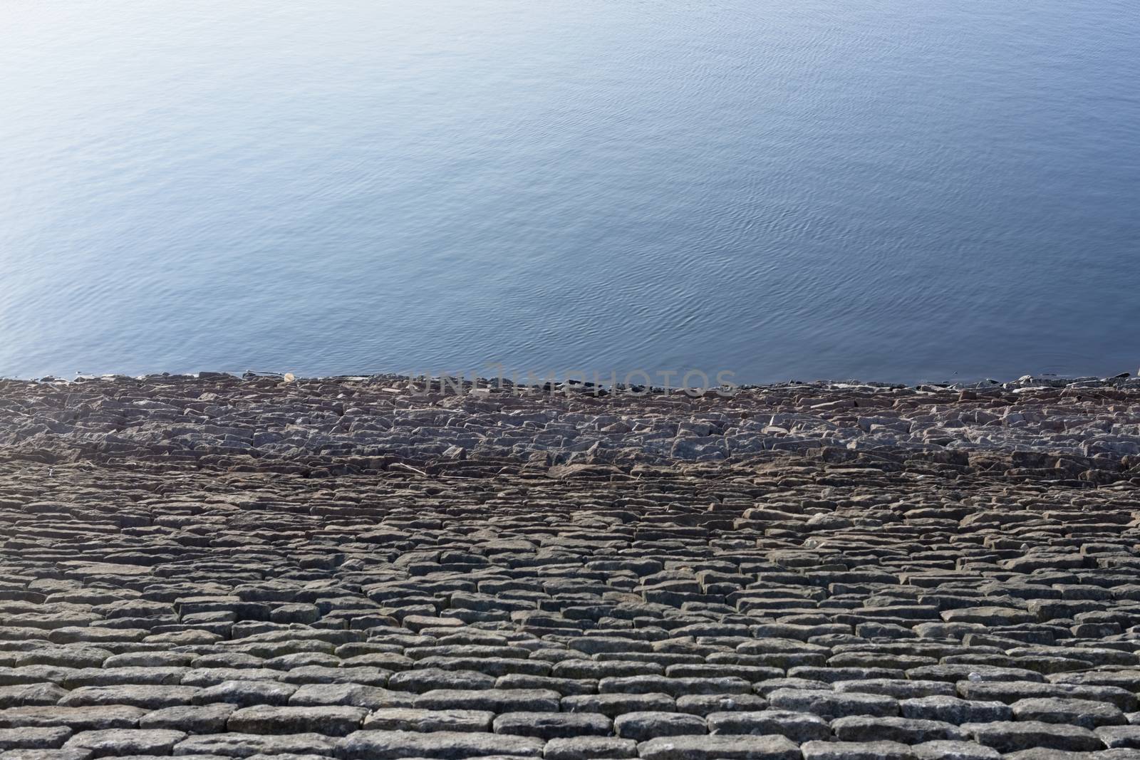 Half and half full frame background texture. Bright blue sunny reservoir water against warm grey linear rock wall. Plain with loads of copy space