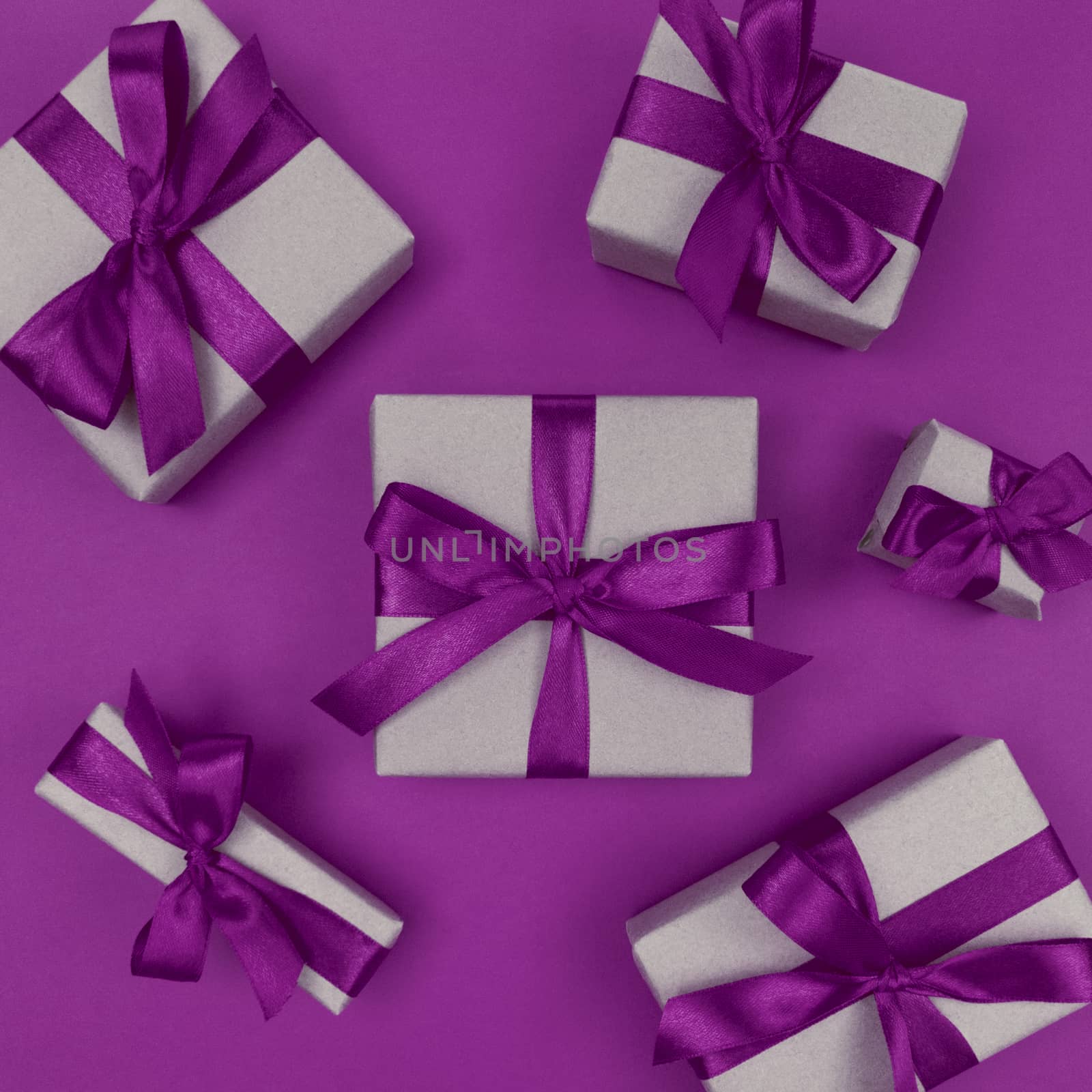 Gift boxes wrapped in a craft paper with purple ribbons and bows. Festive monochrome flat lay.