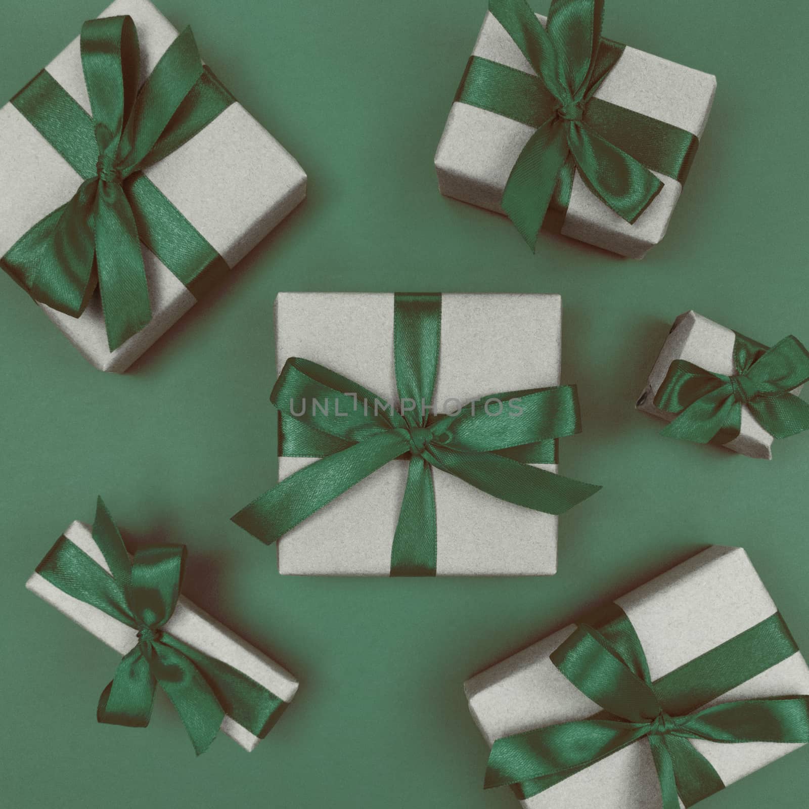 Gift boxes wrapped in a craft paper with green ribbons and bows. Festive monochrome flat lay.