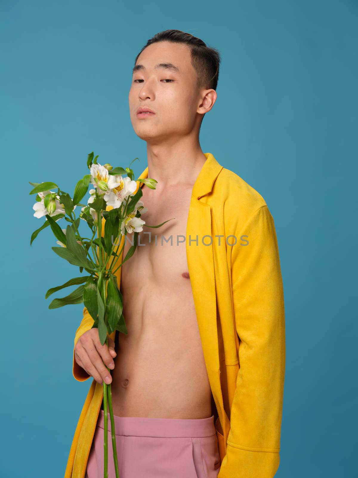 Sexy man in an unbuttoned coat and a bouquet of flowers on a blue background. High quality photo