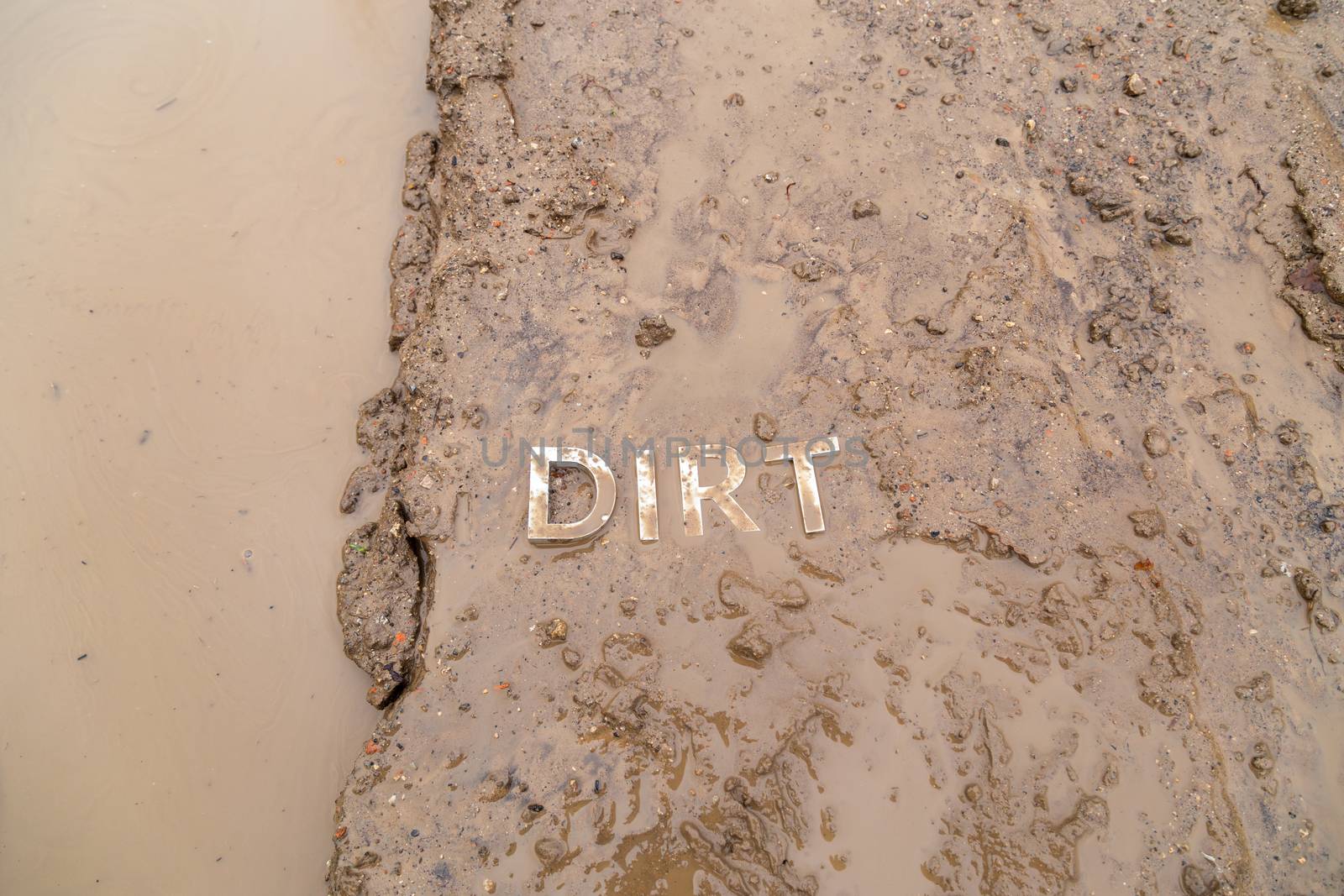 the word mud imprinted in wet dirt road surface and puddle - close-up with selective focus in flat lay perspective.