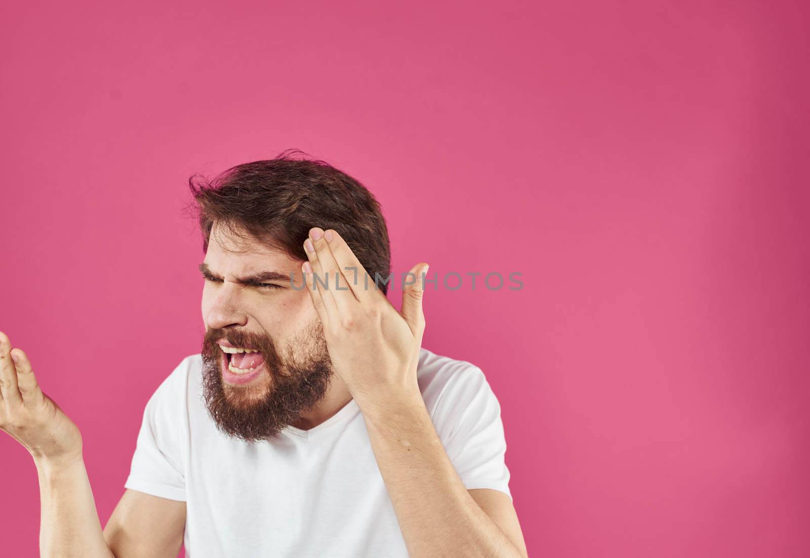 An indignant man gestures with his hands in a white T-shirt on a pink background. High quality photo