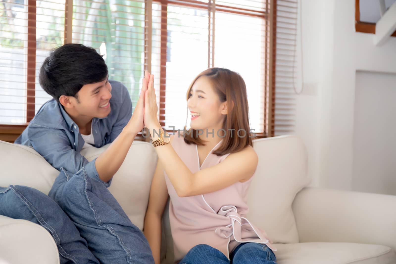 Beautiful young asian couple man and woman gesture hi five together with relax after work success on sofa, family celebration enjoy and excited with happy on couch, lifestyle concept.