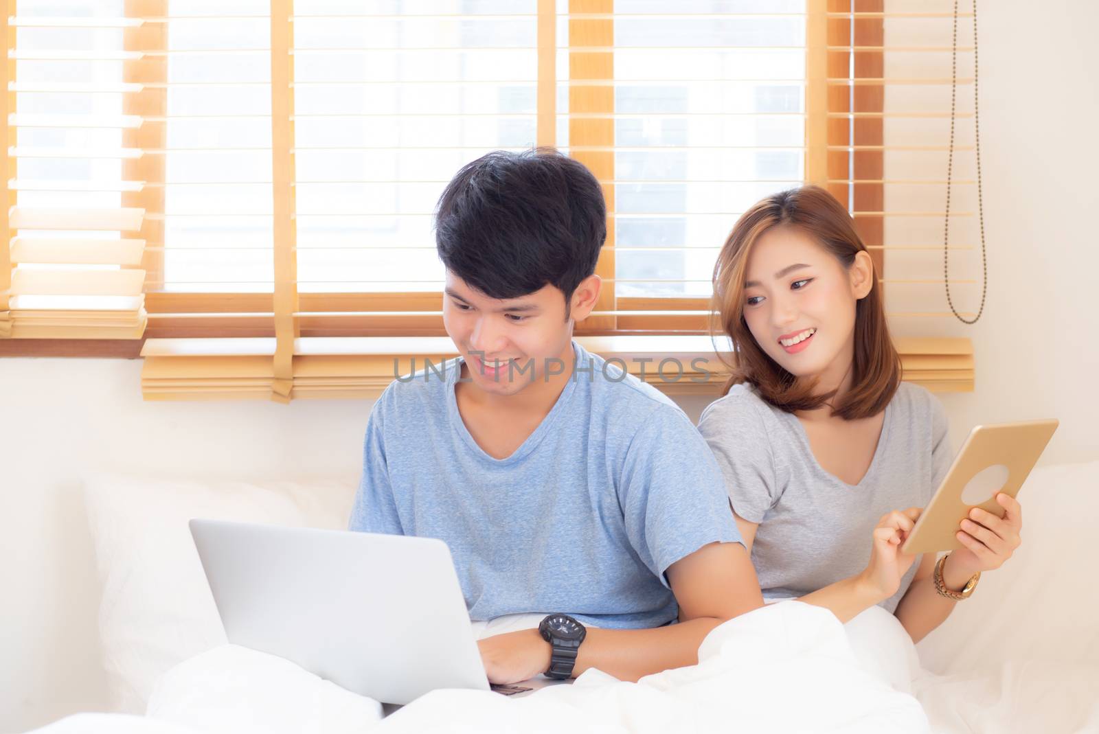 Beautiful young asian couple cheerful freelance working with man using laptop and woman using tablet on couch, family relax and sharing communication together at home, lifestyle concept.