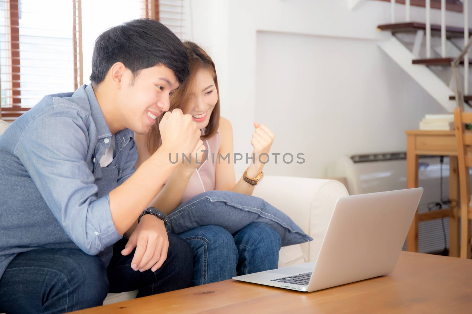 Beautiful portrait asian young couple working laptop with smile and happy sitting on couch at living room, man and woman on sofa using notebook computer with excited, business and success concept.