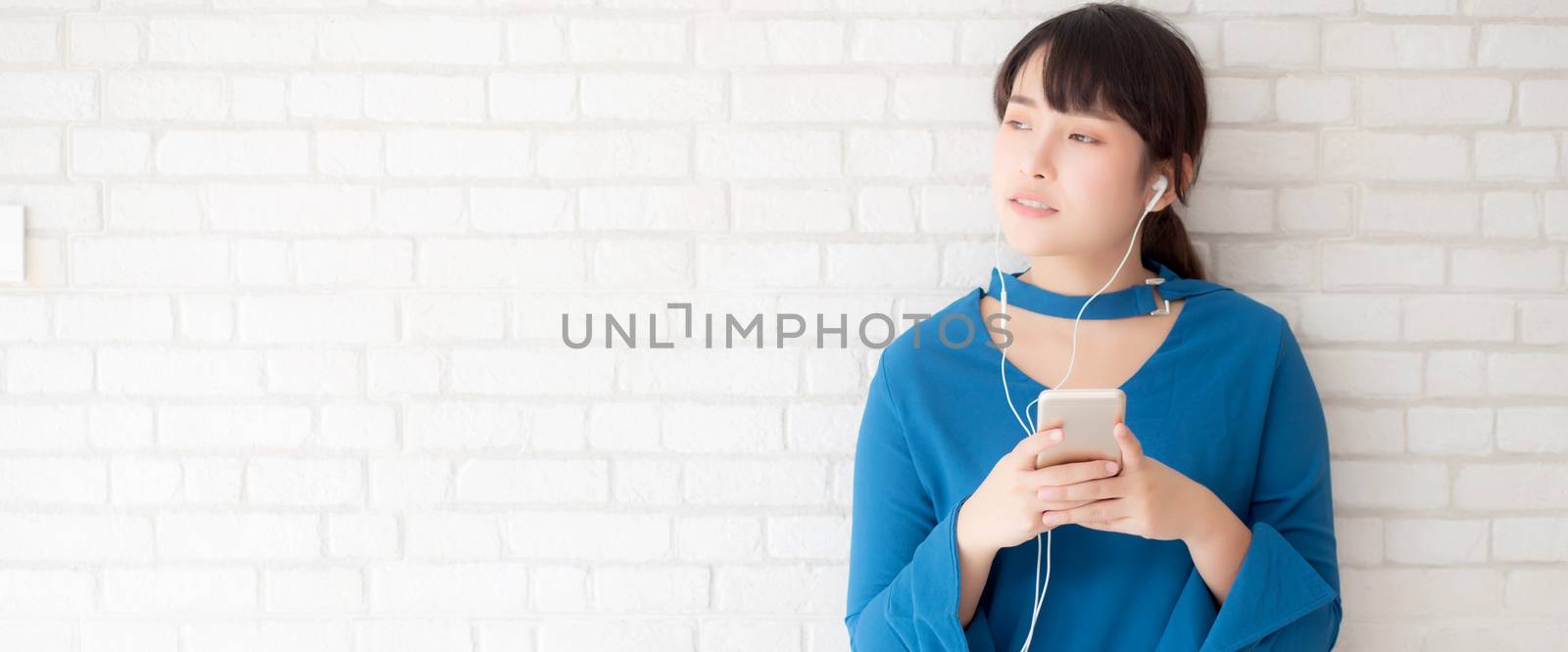 Beautiful portrait asian young woman standing happy enjoy and fun listen music with headphone on cement concrete background, lifestyle of girl relax sound radio with earphone, technology concept.