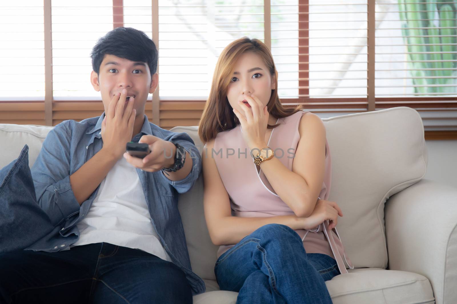 Young asian couple watching horror movie with relax and enjoy holding remote control tv at home, asia man and woman fun surprised and scared together at home, entertainment concept.