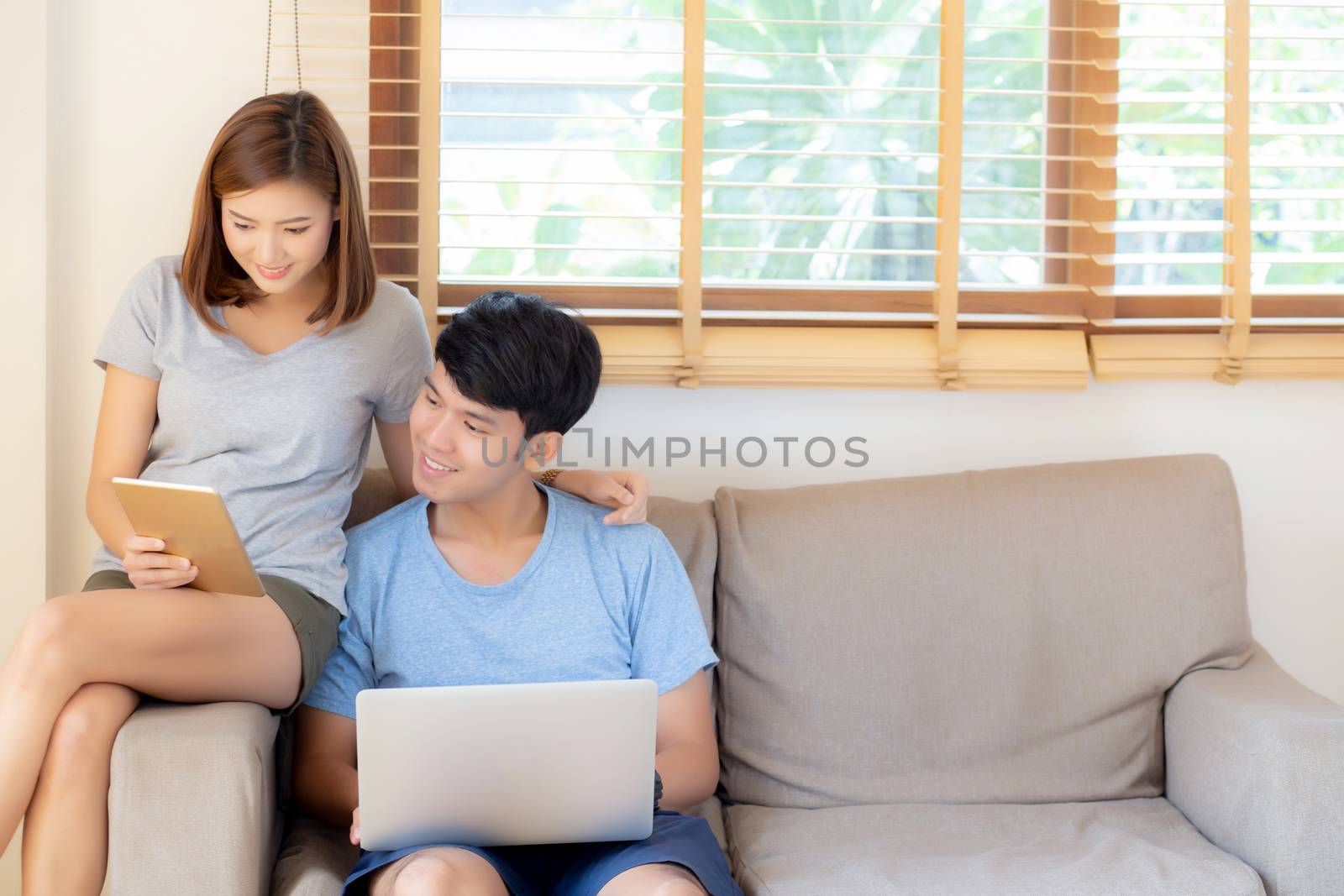 Beautiful young asian couple cheerful freelance working with man using laptop and woman using tablet on couch, family relax and sharing communication together at home, lifestyle concept.