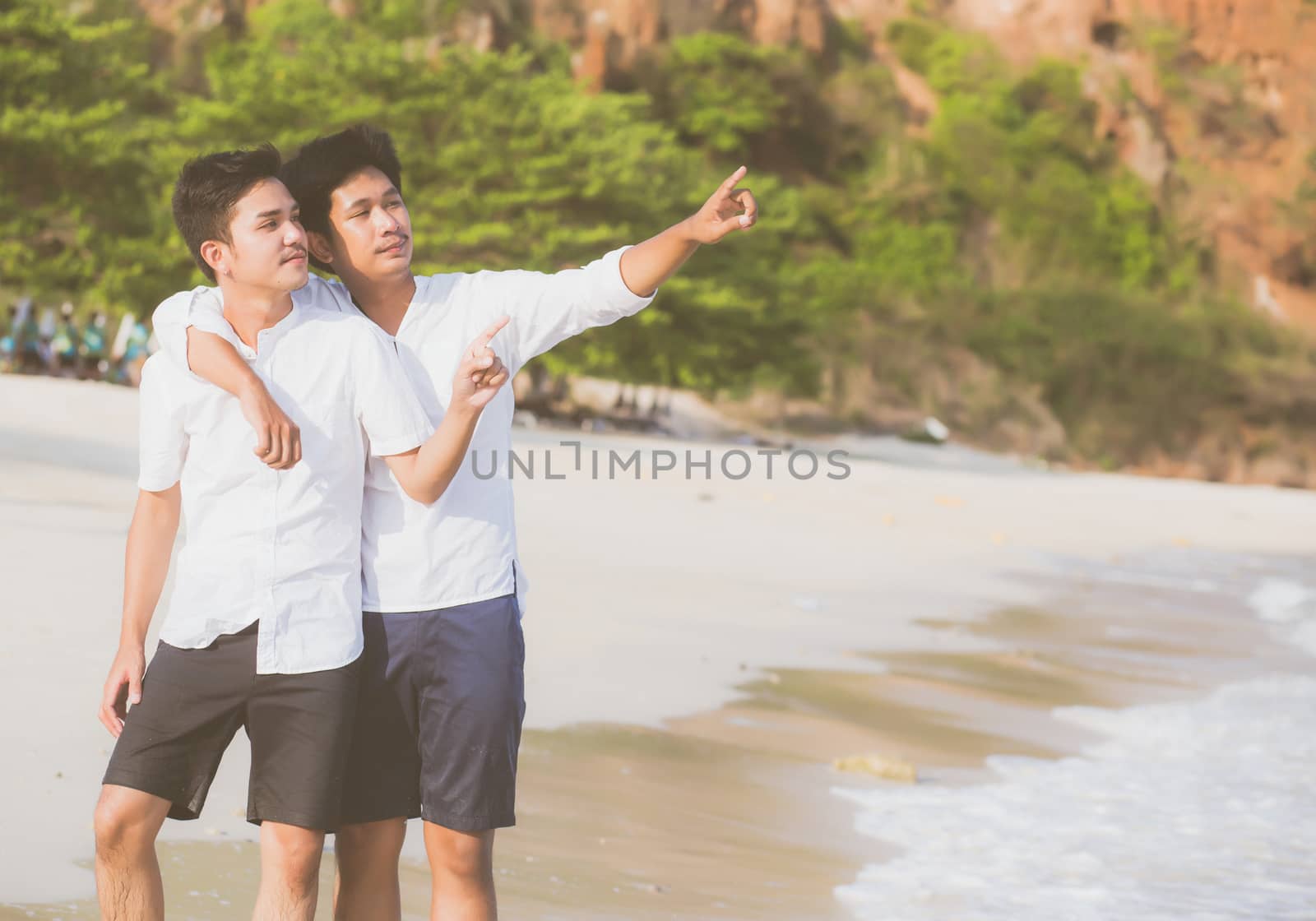 Homosexual portrait young asian couple standing pointing something together on beach in summer, asia gay going sea for leisure with romantic and happy in vacation at sea, LGBT with legal concept.