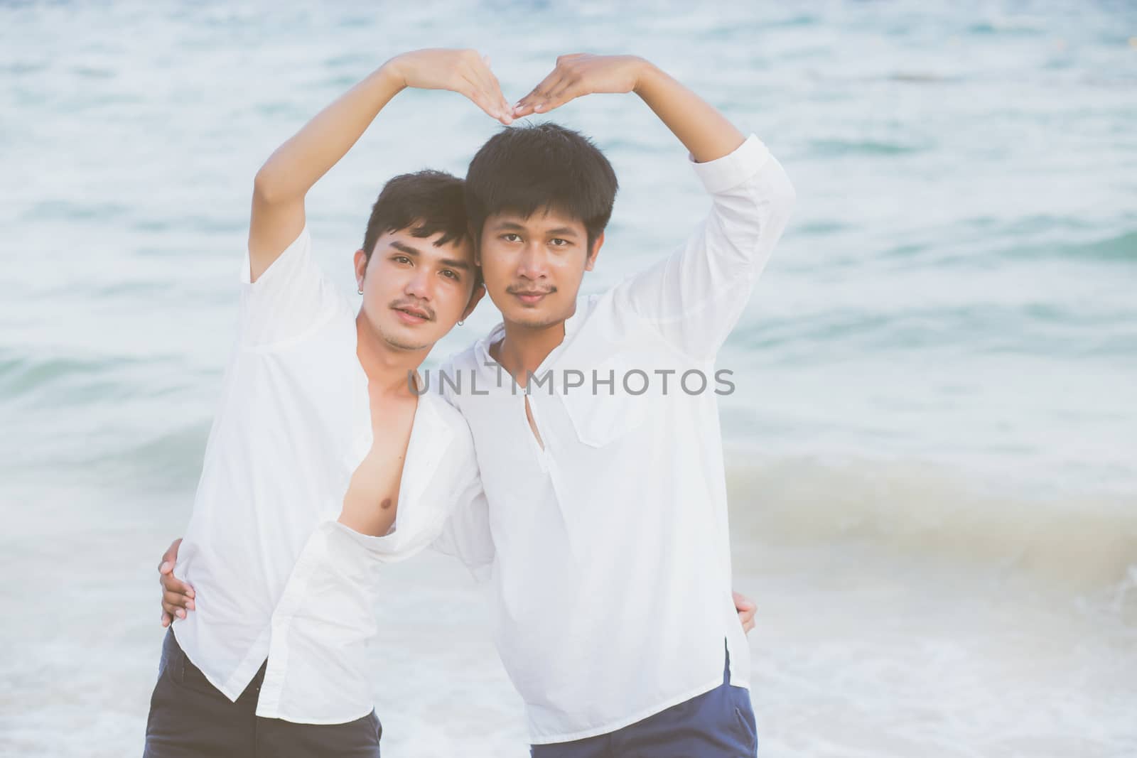 Homosexual portrait young asian couple stand gesture heart shape together on beach in summer, asia gay hug and going sea for leisure with romantic and happy in vacation, LGBT with legal concept.