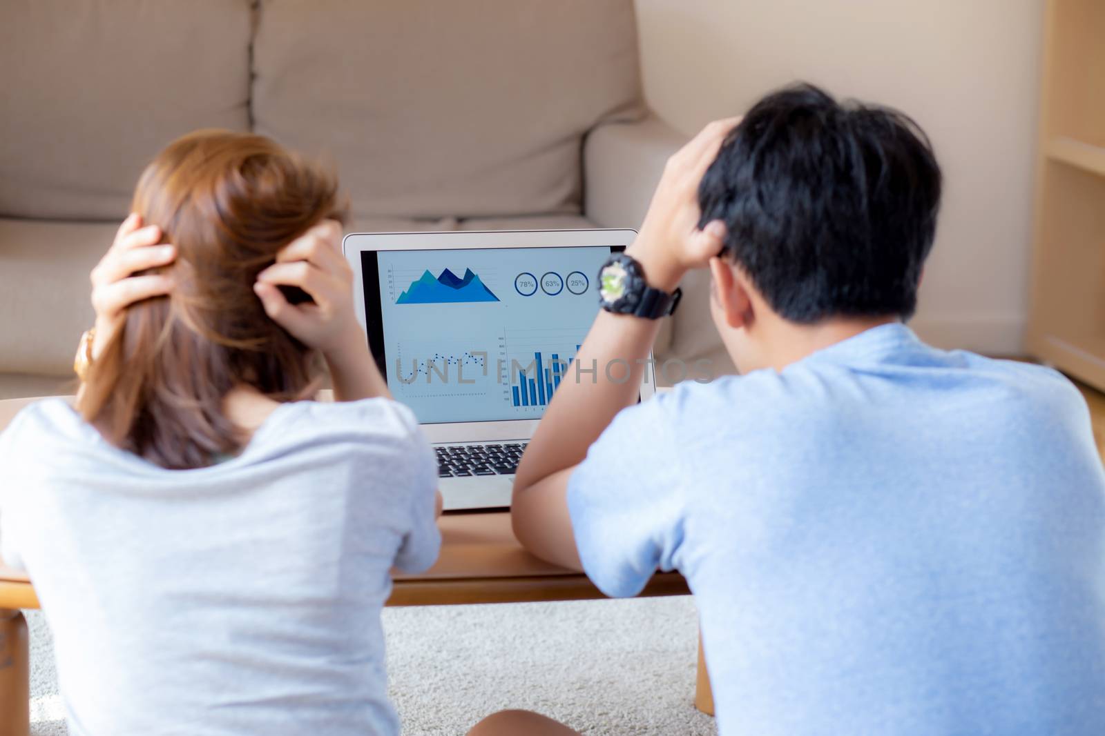 Young asian couple stressed and worried about finance of problem business together, man and woman looking laptop and frustrated about graph and report, family unhappy, lifestyle concept, back view.