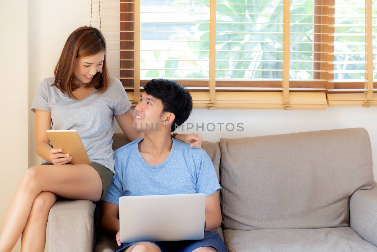 Beautiful young asian couple cheerful freelance working with man using laptop and woman using tablet on couch, family relax and sharing communication together at home, lifestyle concept.