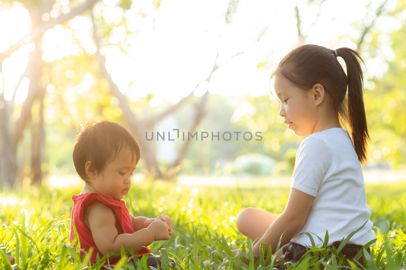 Beautiful young asian kid sitting playing in summer in the park  by nnudoo