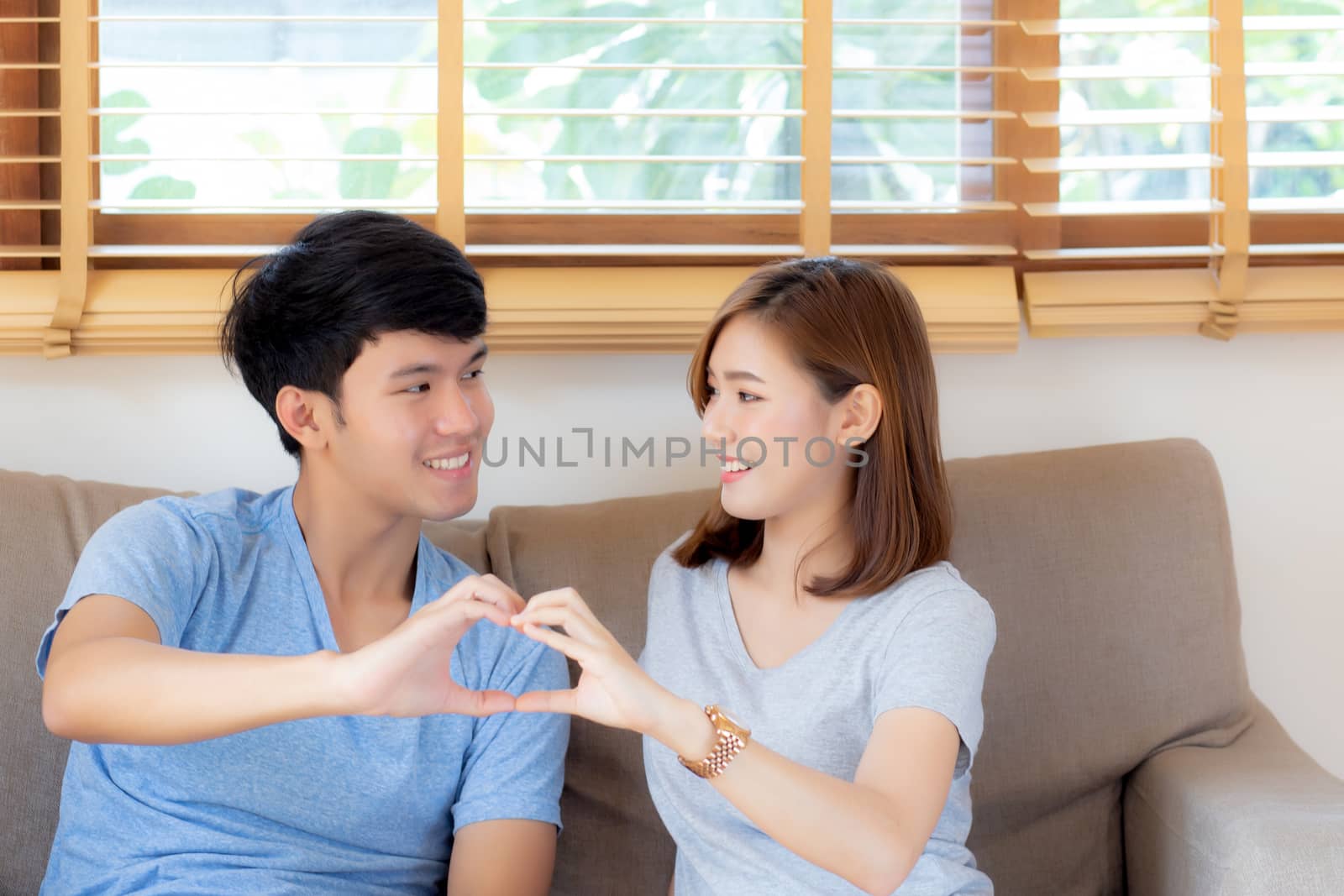 Beautiful happy young couple sitting on sofa fun making gesture  by nnudoo