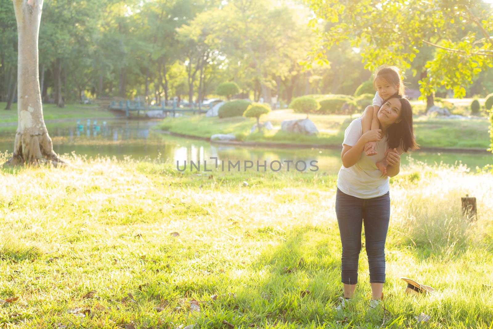 Beautiful young asian mother carrying little daughter with smile, child ride the neck on mom with happiness and cheerful together in the park, lifestyle family with enjoy and fun concept.