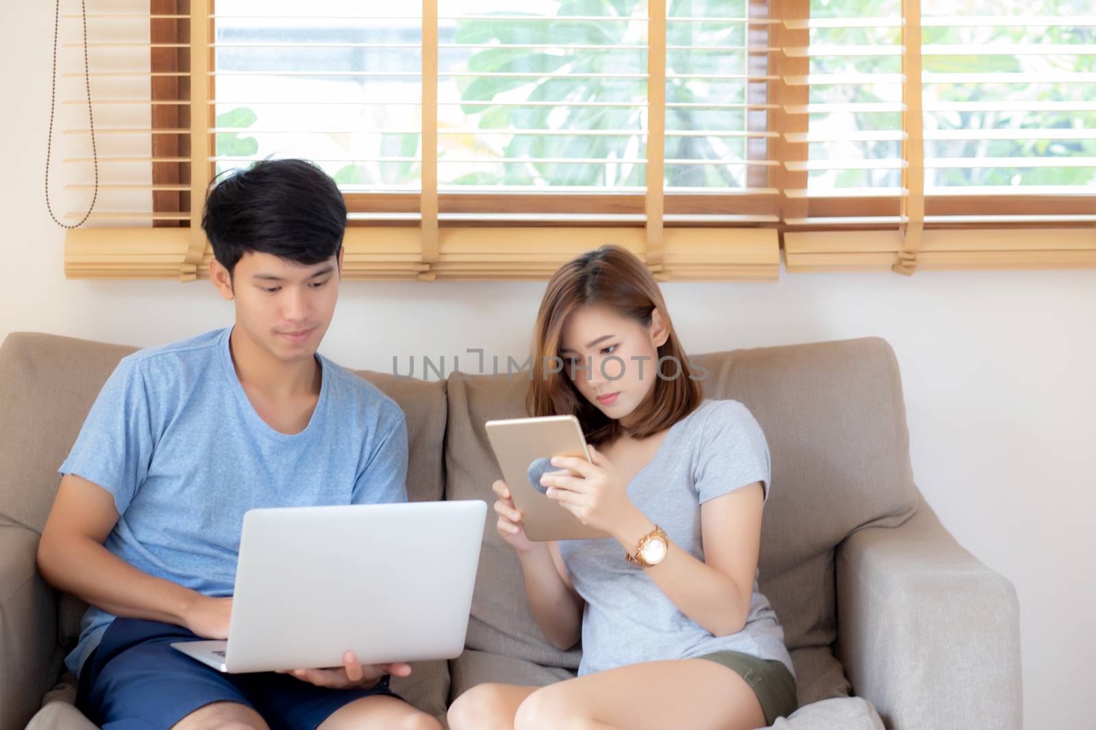 Beautiful young asian couple cheerful freelance working with man using laptop and woman using tablet on couch, family relax and sharing communication together at home, lifestyle concept.