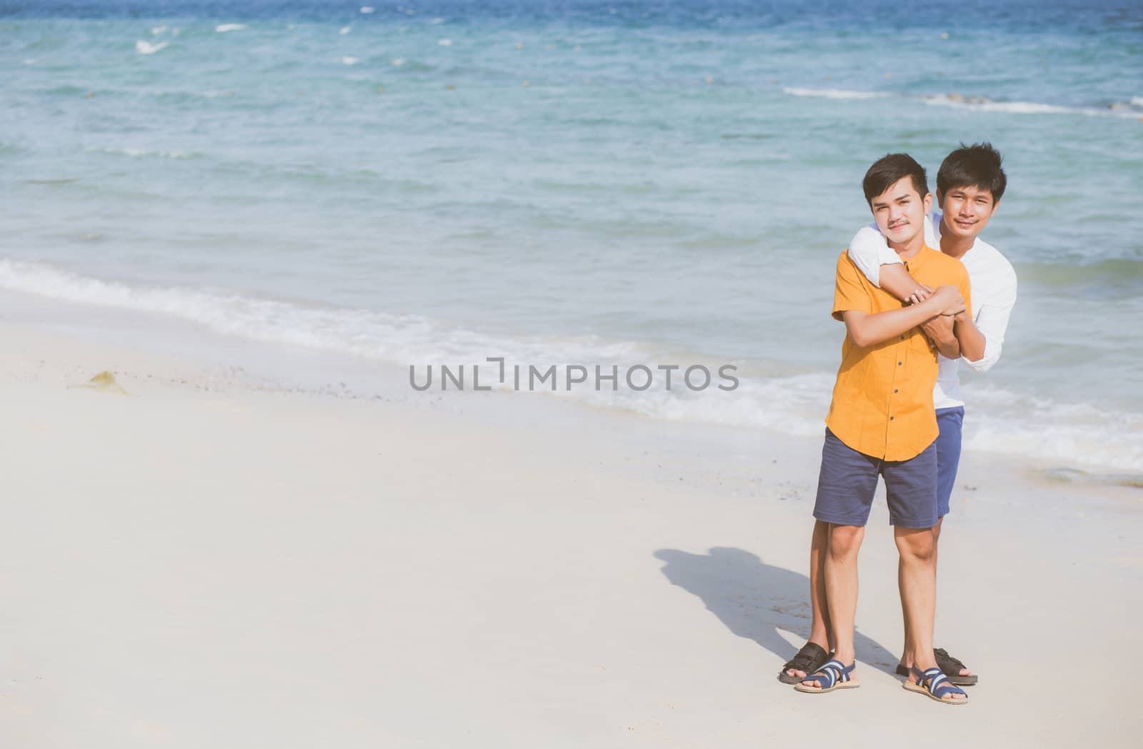 Homosexual portrait young asian couple standing hug together on beach in summer, asia gay going tourism for leisure and relax with romantic and happiness in vacation at sea, LGBT concept.