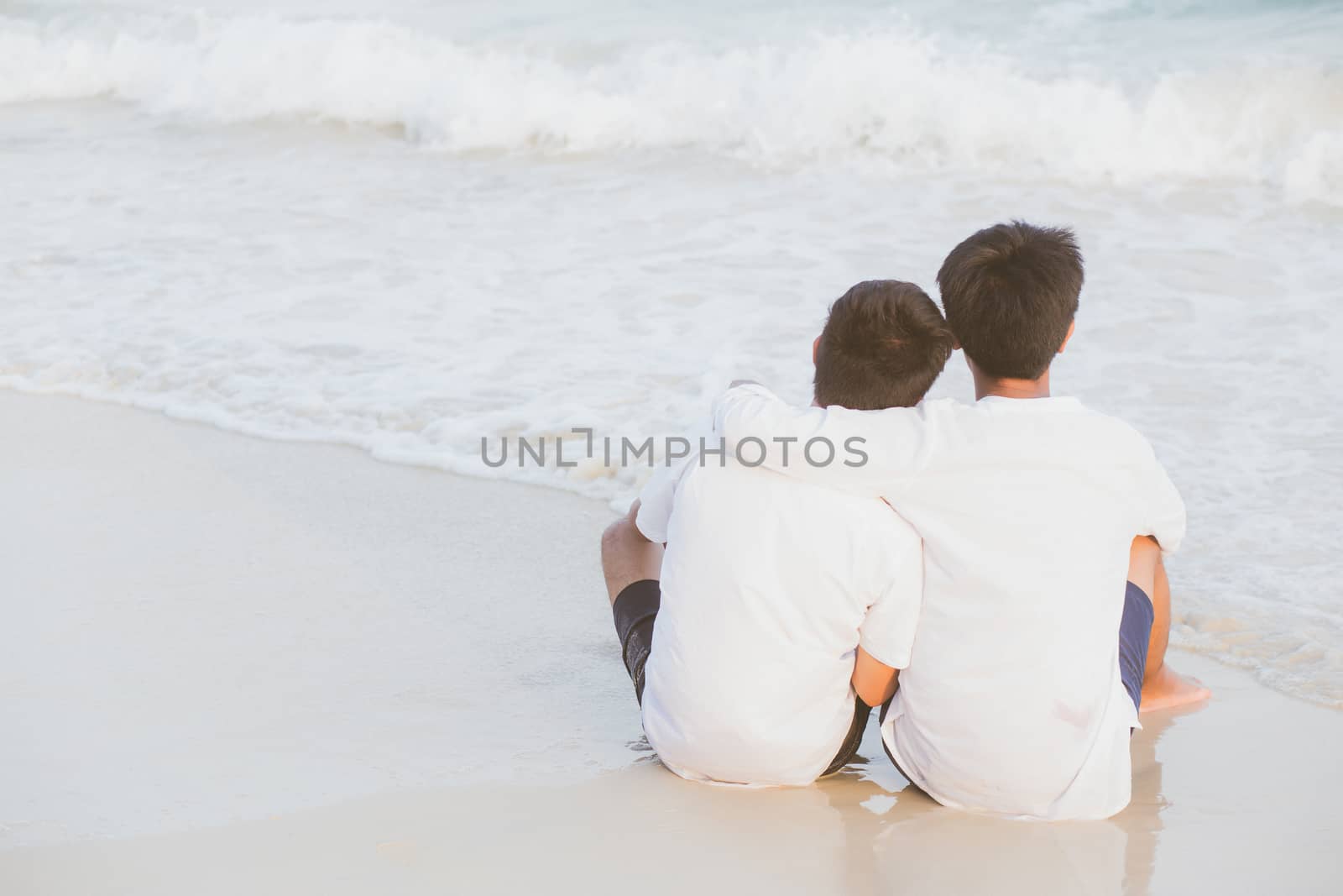 Back view homosexual portrait young asian couple sitting hug together on beach in summer, asia gay going tourism for leisure and relax with romantic and happy in vacation at sea, LGBT legal concept.