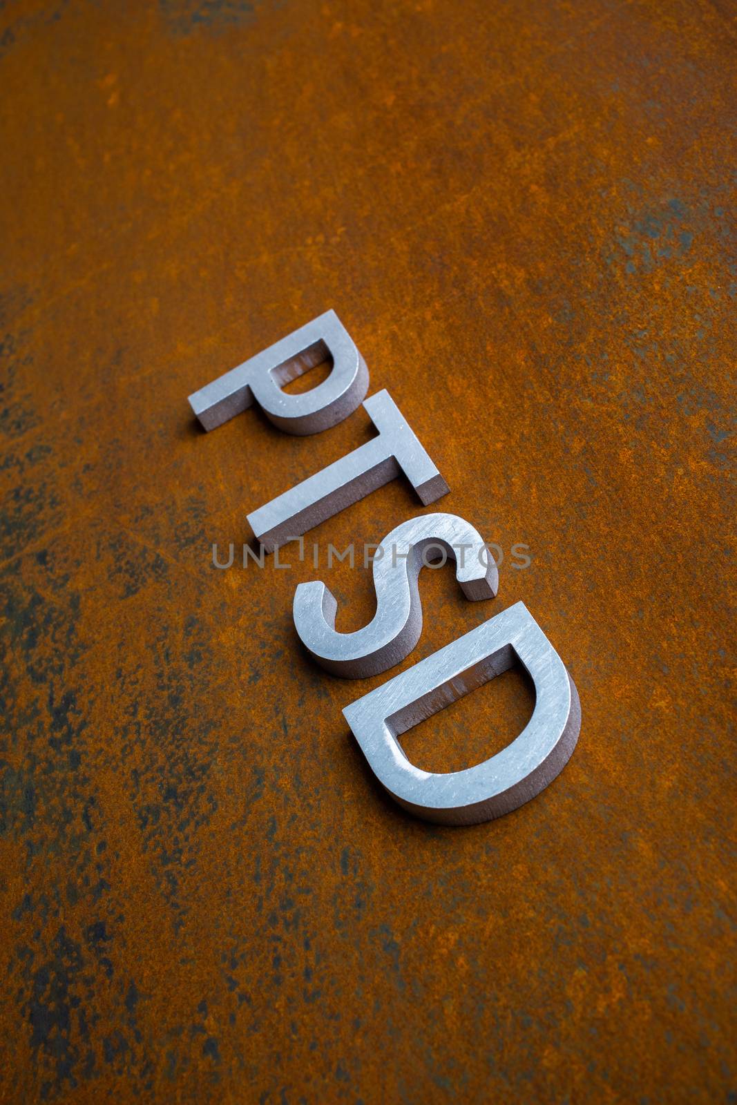 the word PTSD - post traumatic stress disorder - laid with silver metal letters on flat rusted sheet steel background in slanted diagonal perspective.