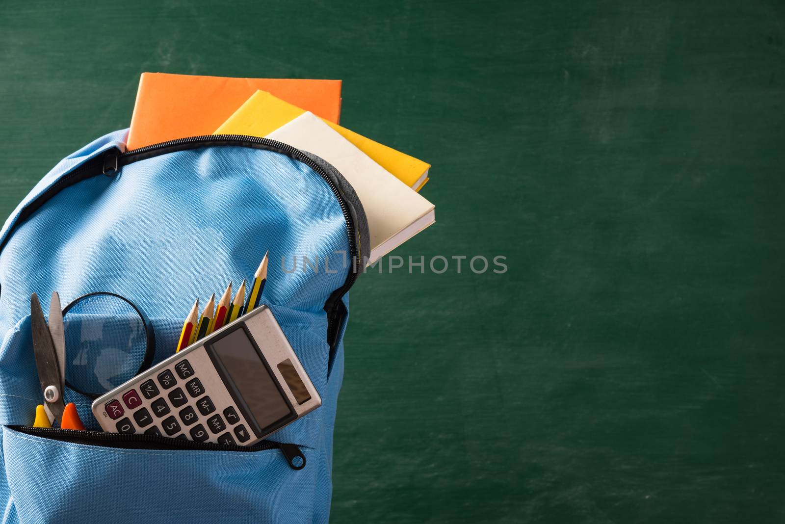 Front of stylish school bag backpack and stationery accessory on a table desk at the green chalkboard, Back to school education concept