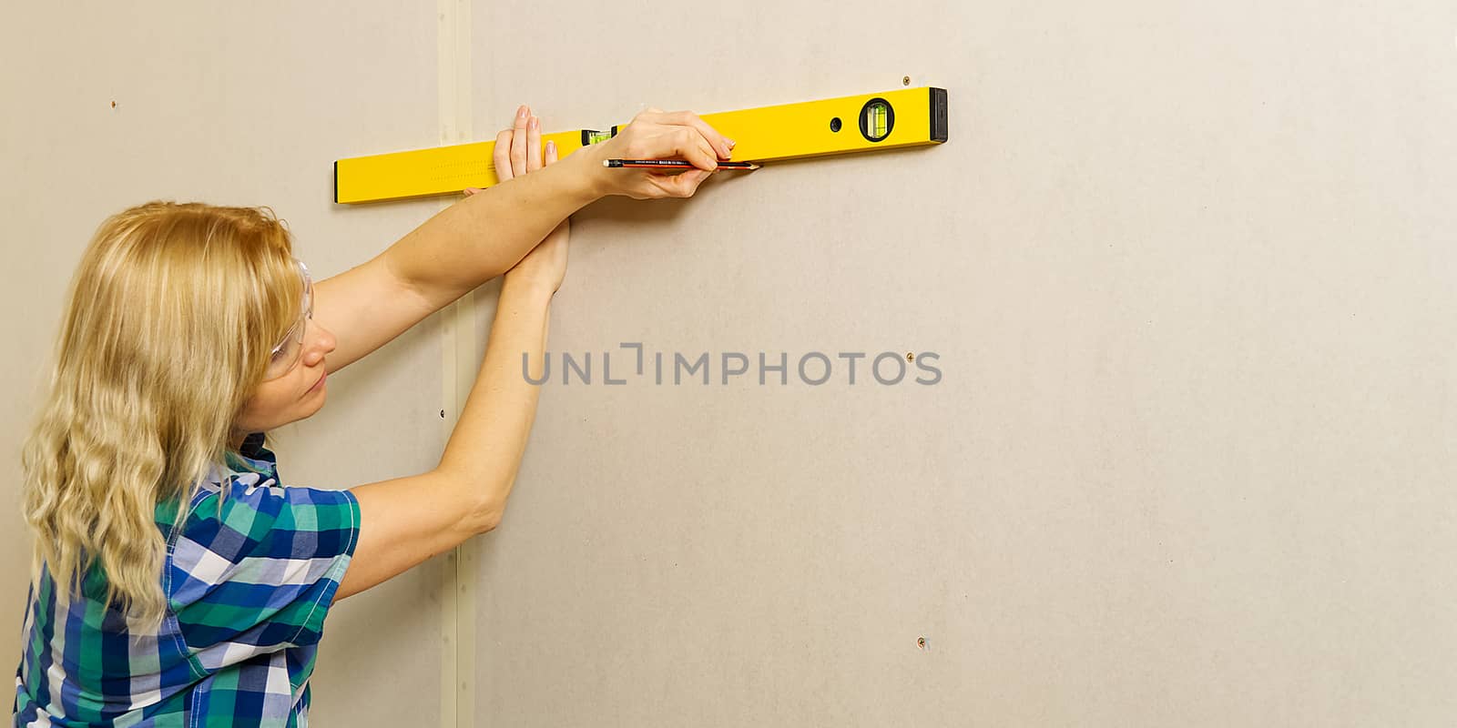 DIY blond young attractive woman using spirit level to work out measurements on plasterboard wall. by PhotoTime