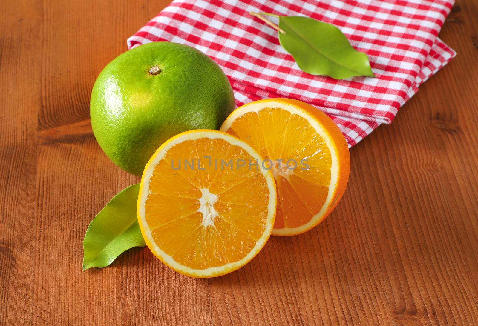 Green grapefruit (sweetie, pomelit, oroblanco), two orange halves and checked red and white tea towel on wooden table