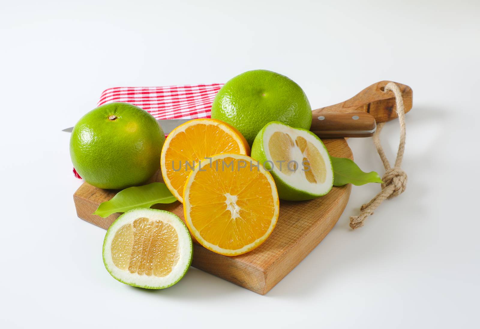 Still life of green grapefruits (sweetie, pomelit, oroblanco grapefruit) and halved orange with knife and tea towel on cutting board