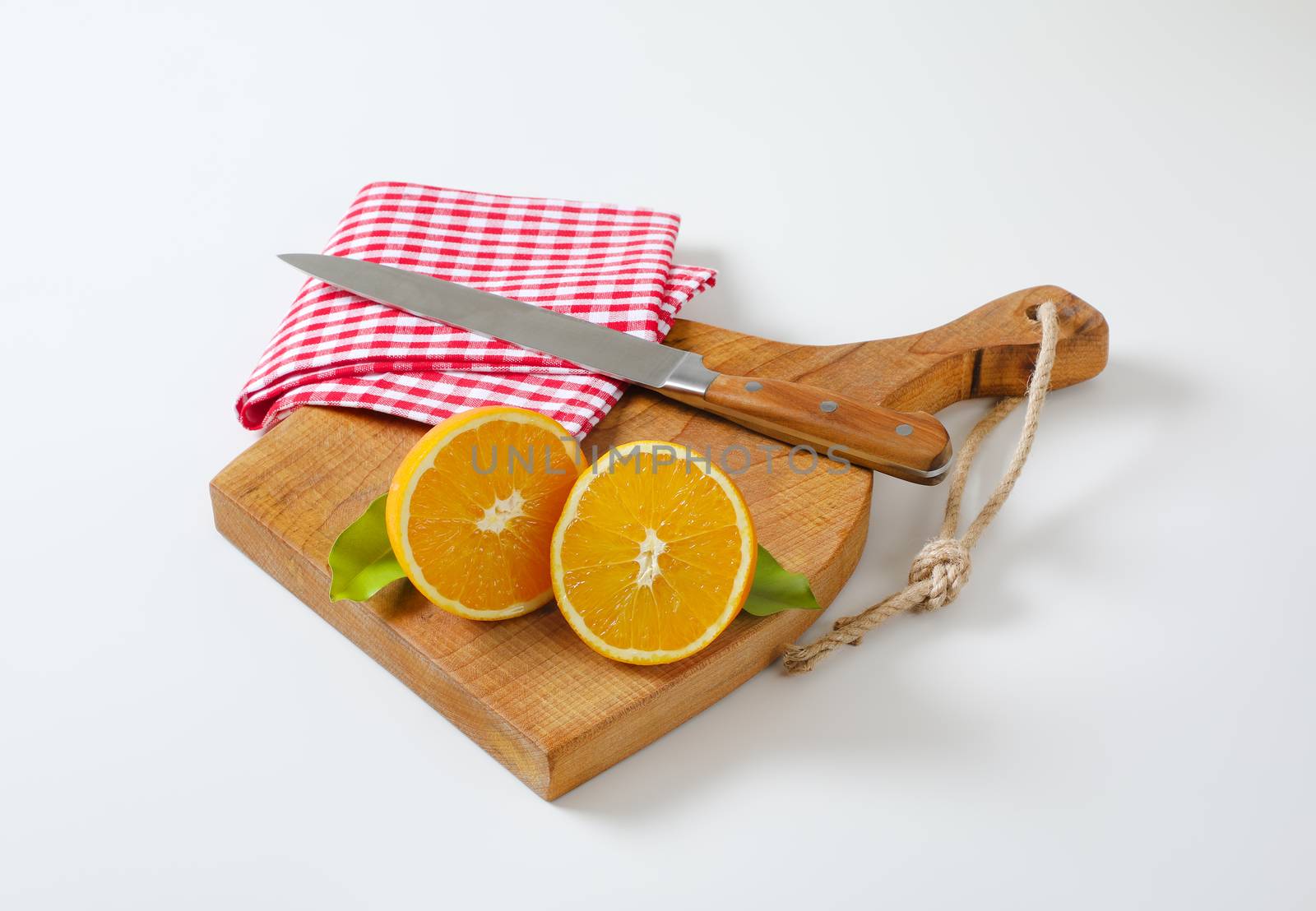 Halved fresh orange, sharp kitchen knife and tea towel on cutting board