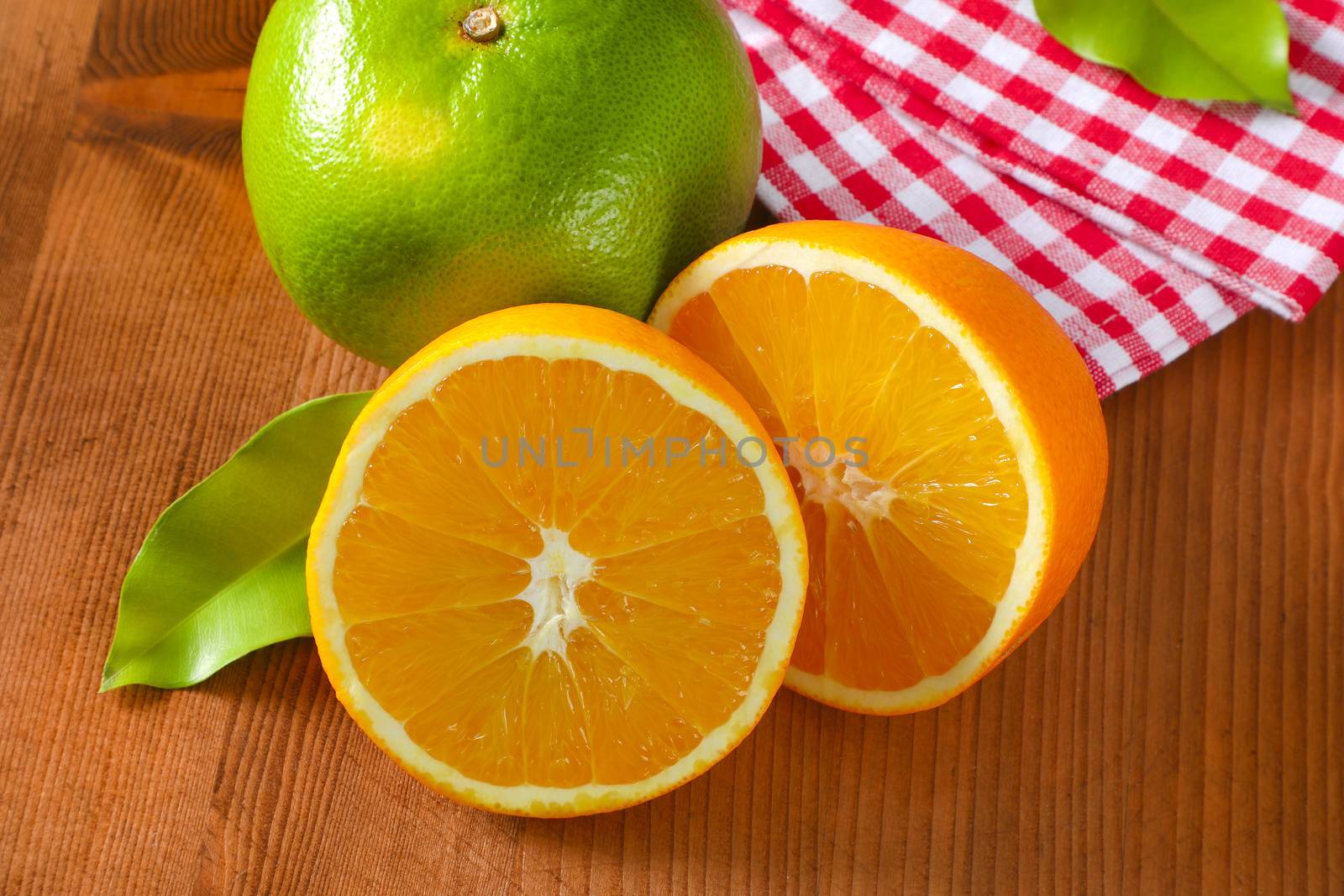 Green grapefruit (sweetie, pomelit, oroblanco), two orange halves and checked red and white tea towel on wooden table