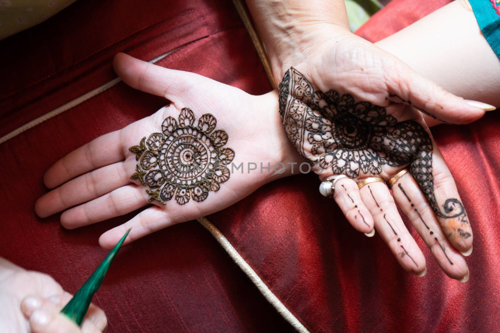 Top down video of a woman copying the mehndi henna tattoo from one hand to the other in preparation of the hindu festival of teej, karwachauth, diwali dussera or a marriage function. Shot in natural light on a beautiful red background it shows the amazing artistry of make up artists who make these beautiful and intricate designs