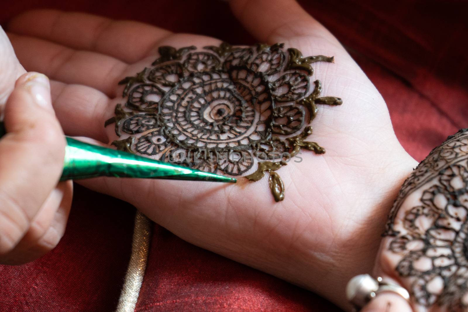 Close up macro shot of mehendi henna tattoo being applied in an intricate pattern on the hand of a woman with soft natural light and on a red background on the event of karwachauth marriage shaadi. Shows the very popular temporary tattoo method that is a part of the hindu religion and is widely done across india