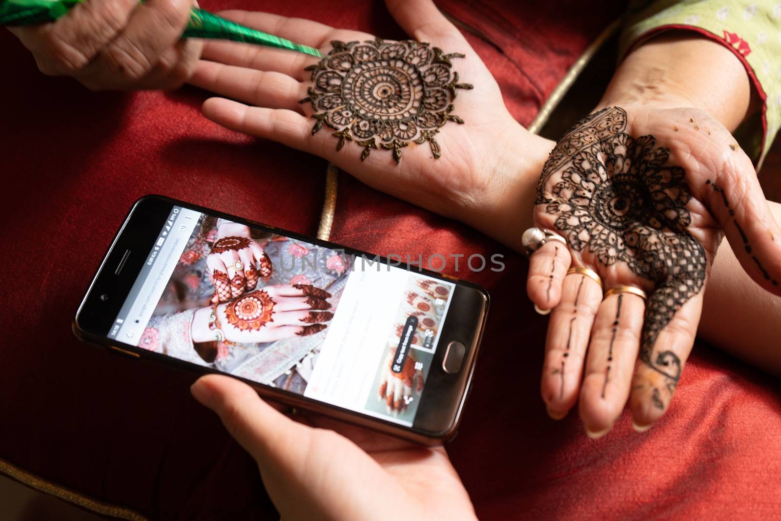 Woman getting a henna tattoo mehendi design copied from phone onto her hand for the bride bridesmaid shaadi event or a hindu festival like karwachauth diwali holi and teej. Shows the very popular temporary tattoo method that is a part of the hindu religion and is widely done across india