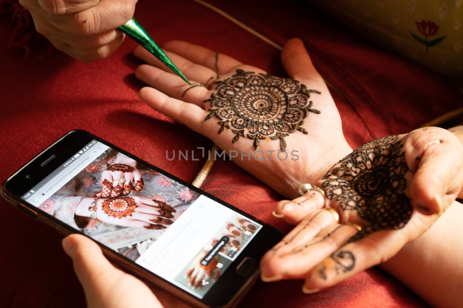 Woman getting a henna tattoo mehendi design copied from phone onto her hand for the bride bridesmaid shaadi event or a hindu festival like karwachauth diwali holi and teej by Shalinimathur