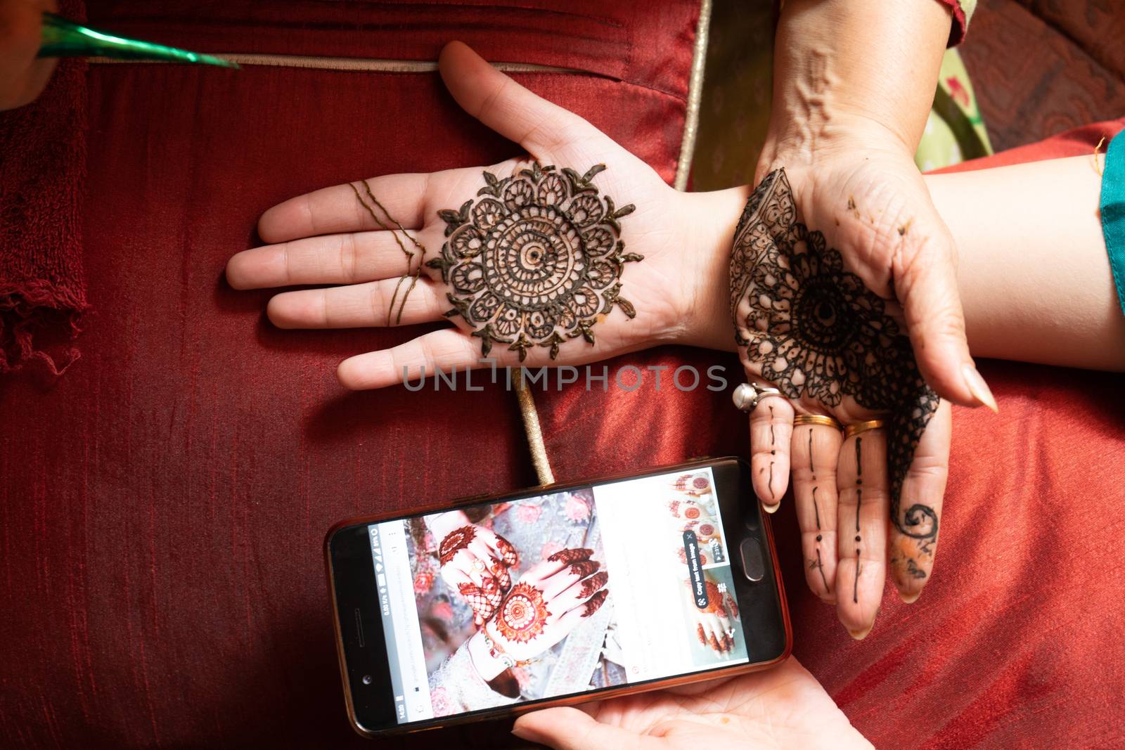 Woman getting a henna tattoo mehendi design copied from phone onto her hand for the bride bridesmaid shaadi event or a hindu festival like karwachauth diwali holi and teej by Shalinimathur