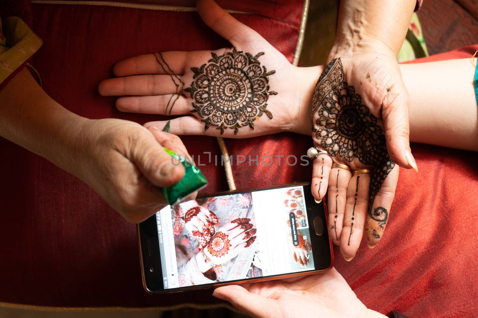 Woman getting a henna tattoo mehendi design copied from phone onto her hand for the bride bridesmaid shaadi event or a hindu festival like karwachauth diwali holi and teej by Shalinimathur