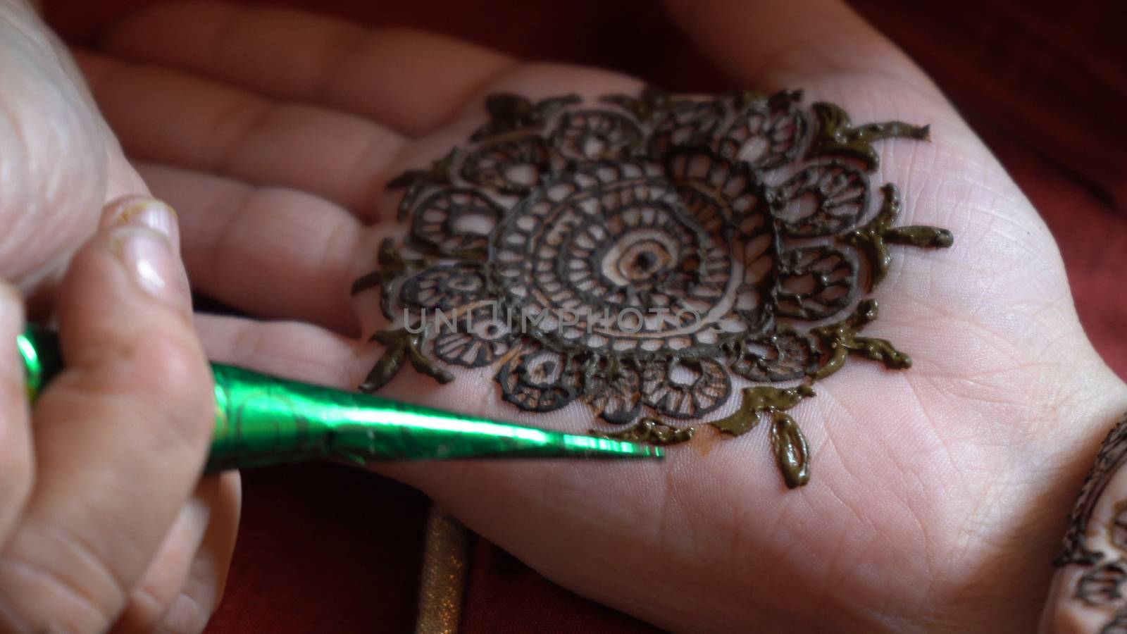 Close up macro shot of mehendi henna tattoo being applied in an intricate pattern on the hand of a woman with soft natural light and on a red background on the event of karwachauth marriage shaadi by Shalinimathur