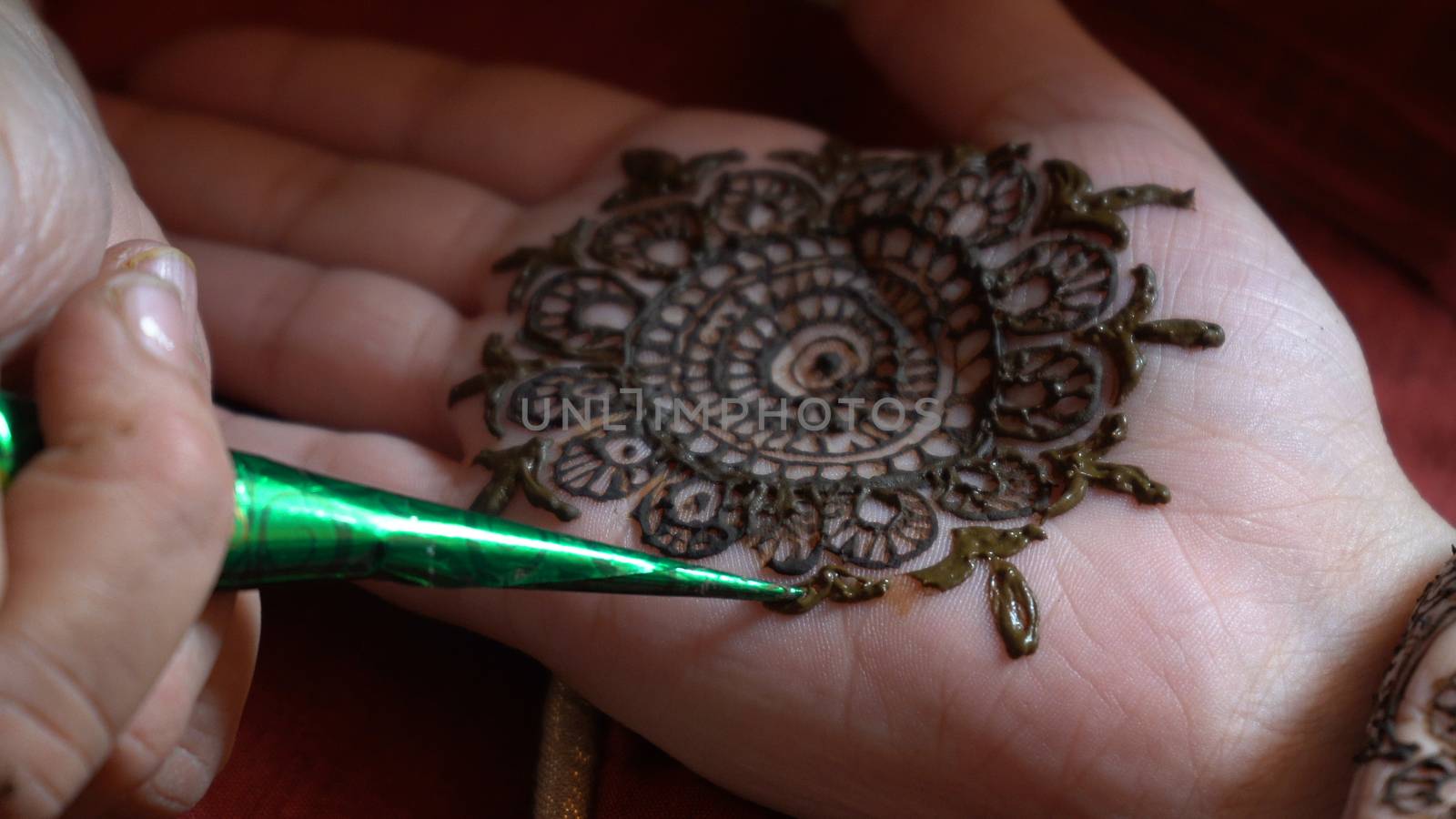 Close up macro shot of mehendi henna tattoo being applied in an intricate pattern on the hand of a woman with soft natural light and on a red background on the event of karwachauth marriage shaadi by Shalinimathur