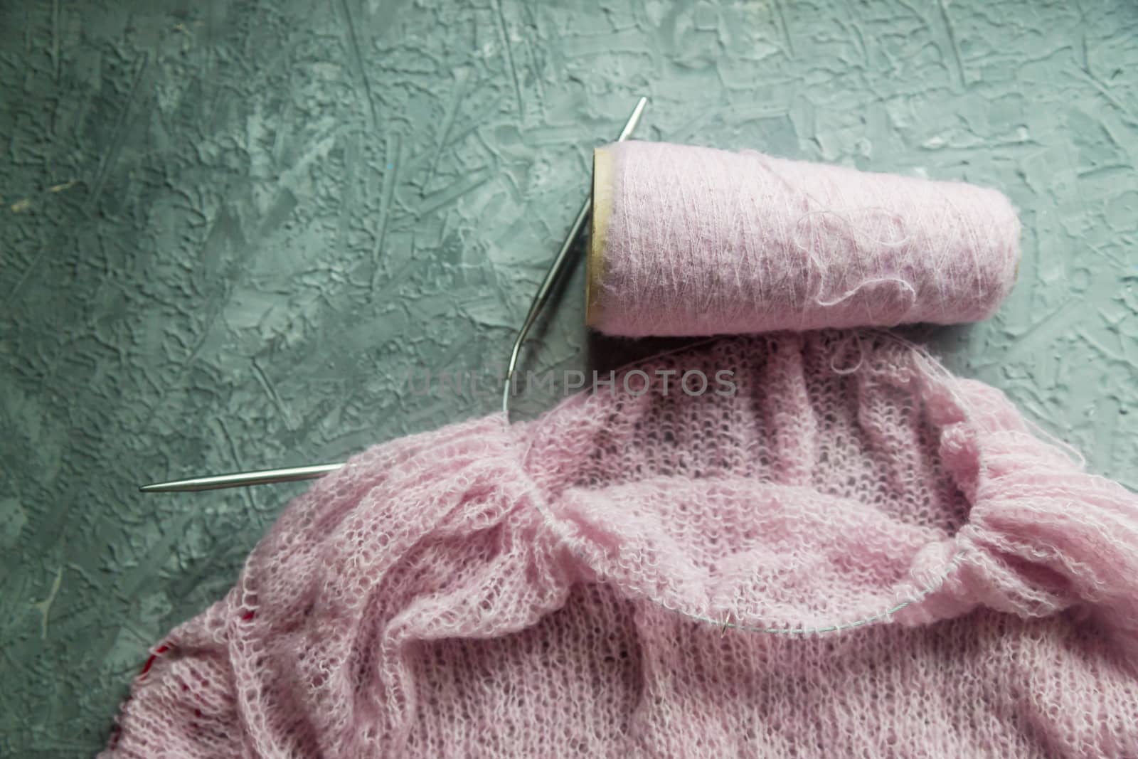 Knitting background flatlay. Bobbin of pink yarn, knitting needles, a knitted pullover on a concrete background, top view. Background about needlework and handicrafts, copy space