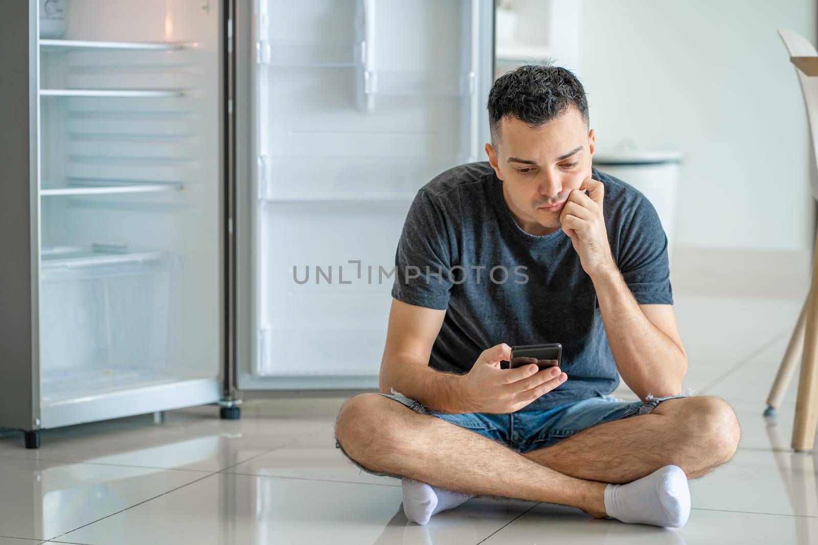 A young guy orders food using a smartphone. Empty refrigerator with no food. Food delivery service advertisement.