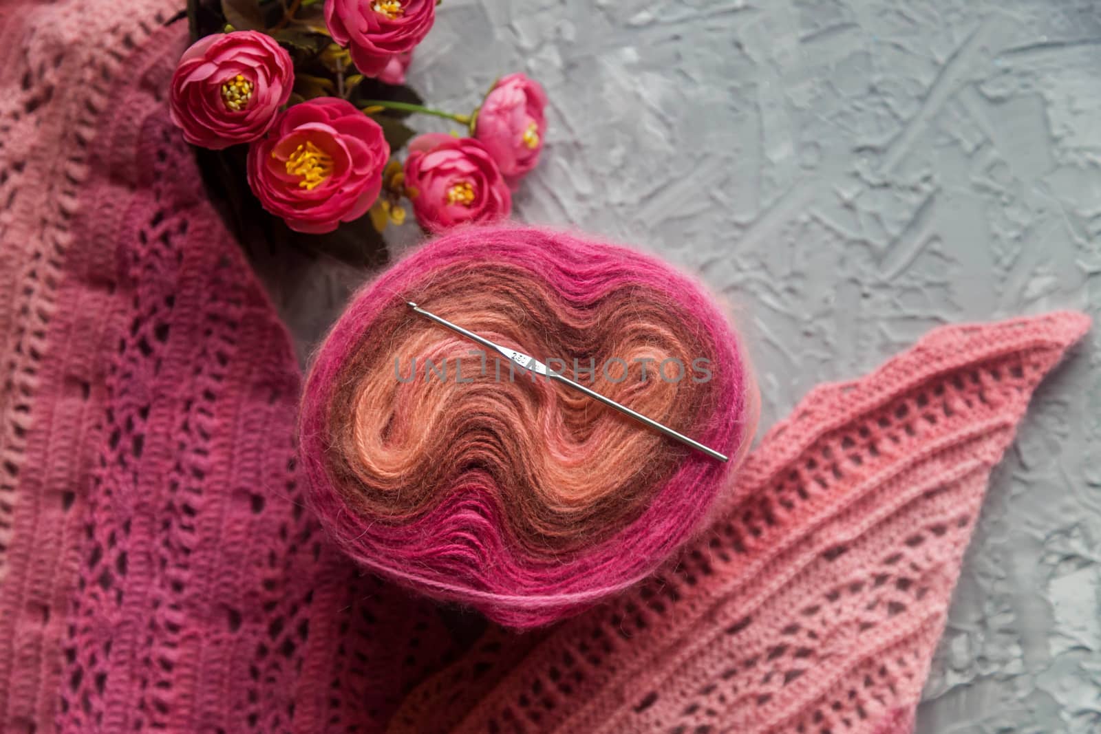 Crochet background flatlay. Bobbin of colored yarn, crochet hook, crochet scarf on a concrete background, top view. Background about needlework and handicrafts, copy space