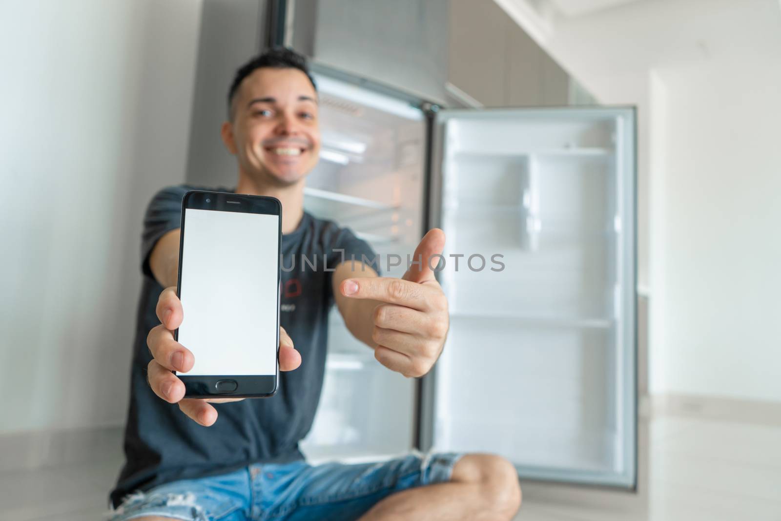 A young guy orders food using a smartphone. Empty refrigerator with no food. Food delivery service advertisement.