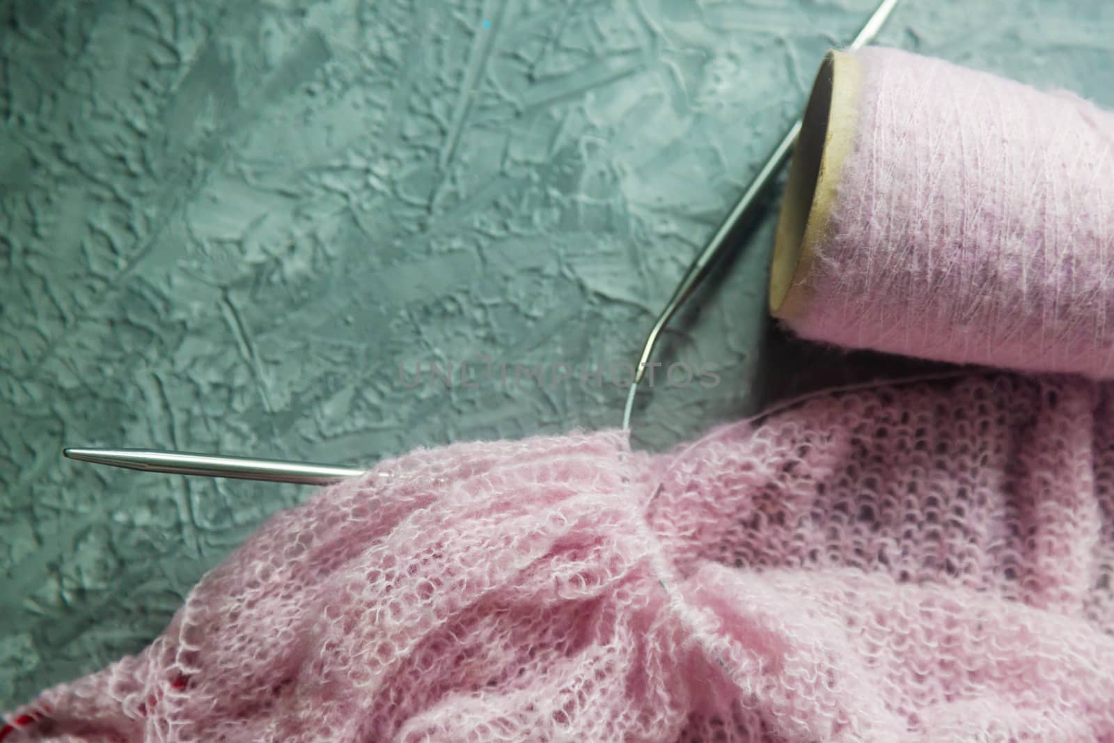 Knitting background flatlay. Bobbin of pink yarn, knitting needles, a knitted pullover on a concrete background, top view. Background about needlework and handicrafts, copy space