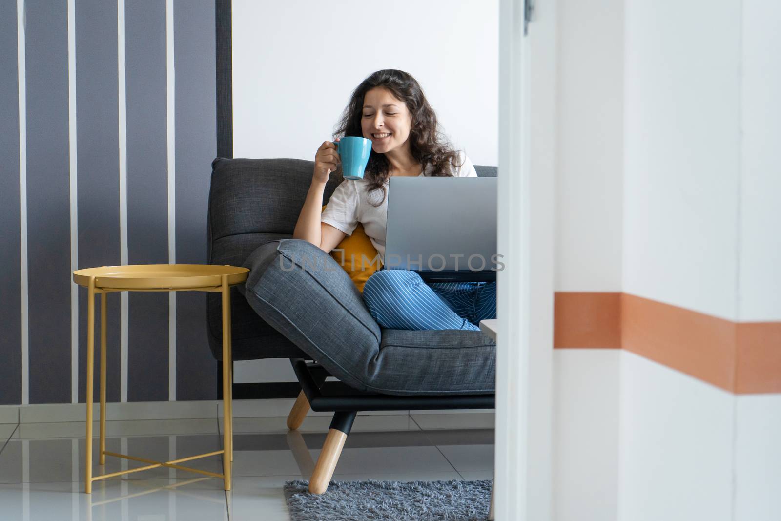 Beautiful girl sitting with a laptop on a sofa in a stylish room. Work from home. Work atmosphere in a good mood.