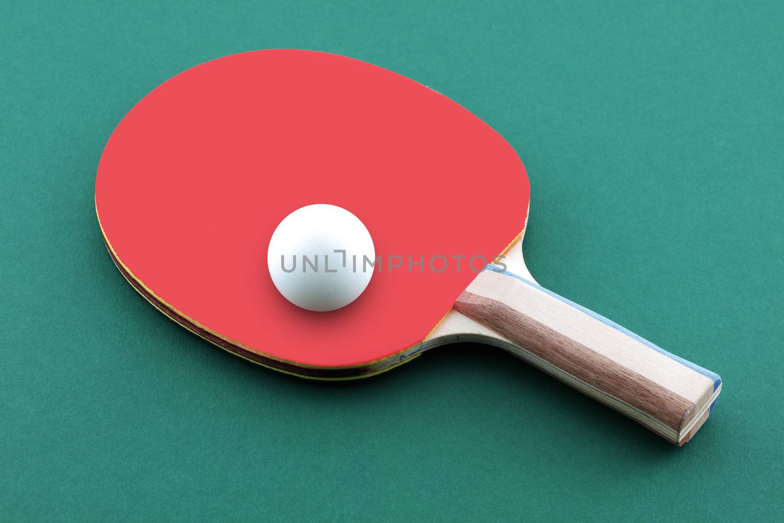 A green ping pong table with ball resting on a table tennis bat paddle