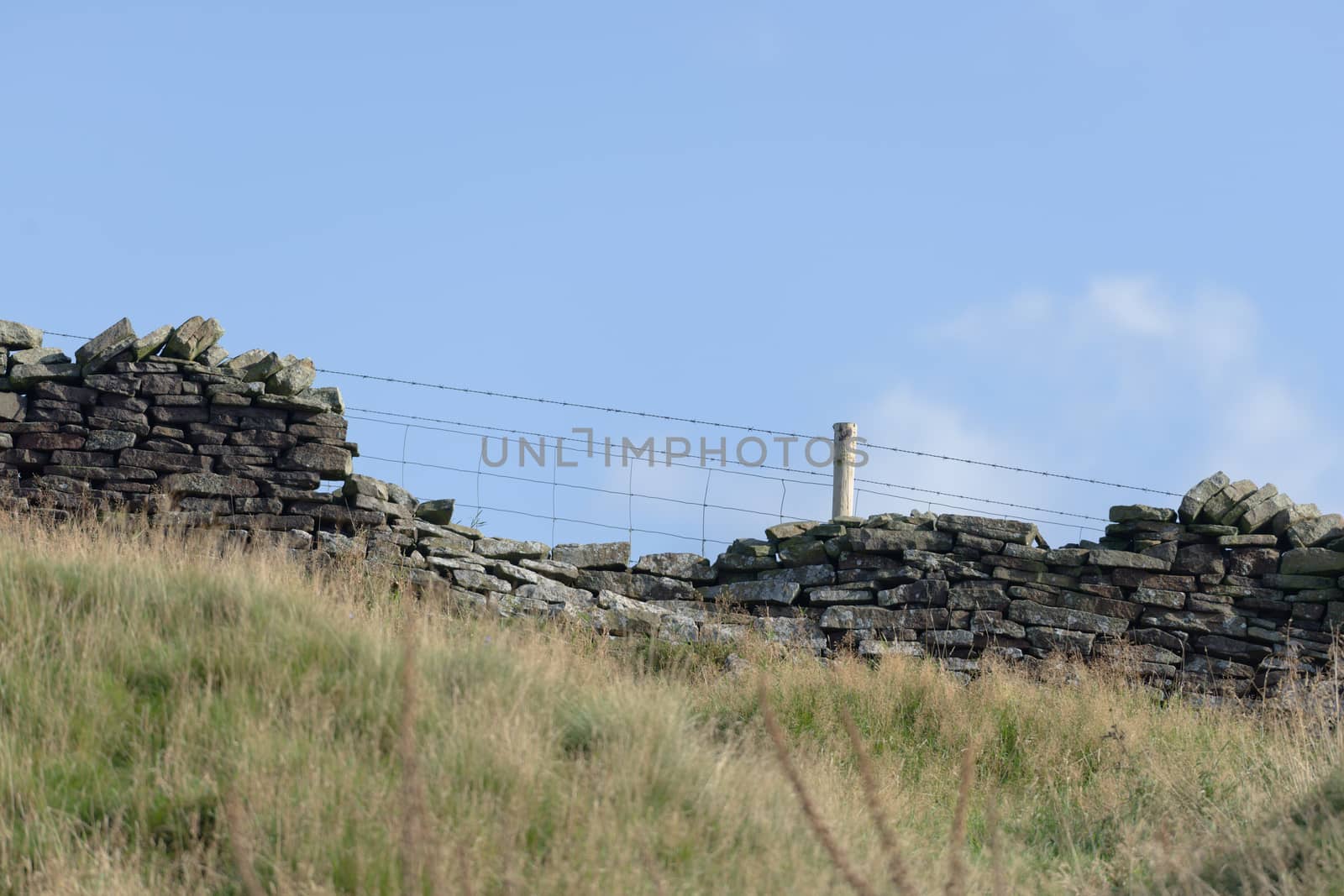 Profile of drystone wall and barbed wire fence against pastel blue sky background. Autumn rural season in the peak district, selective focus texture.