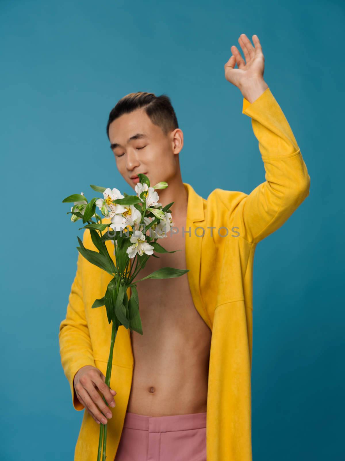 Cute young man in a yellow coat and white flowers blue background holidays . High quality photo
