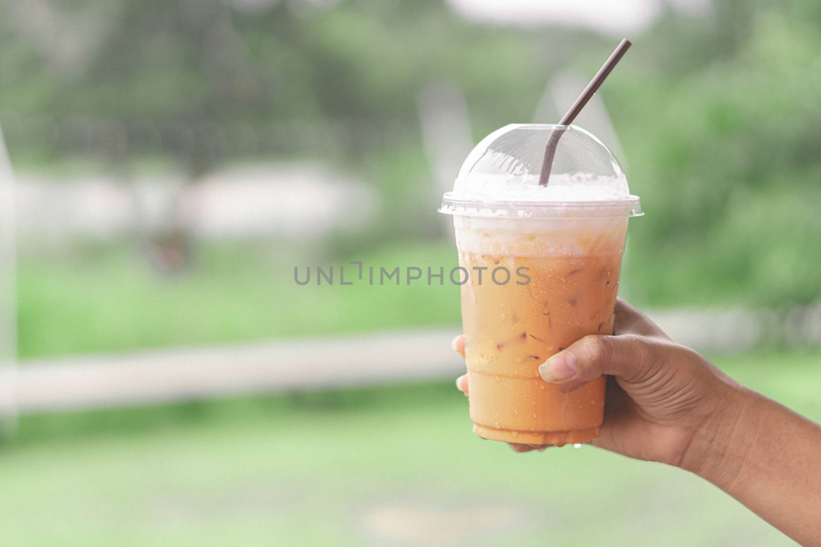Closeup woman hand holding thai milk tea on wood table with nature background