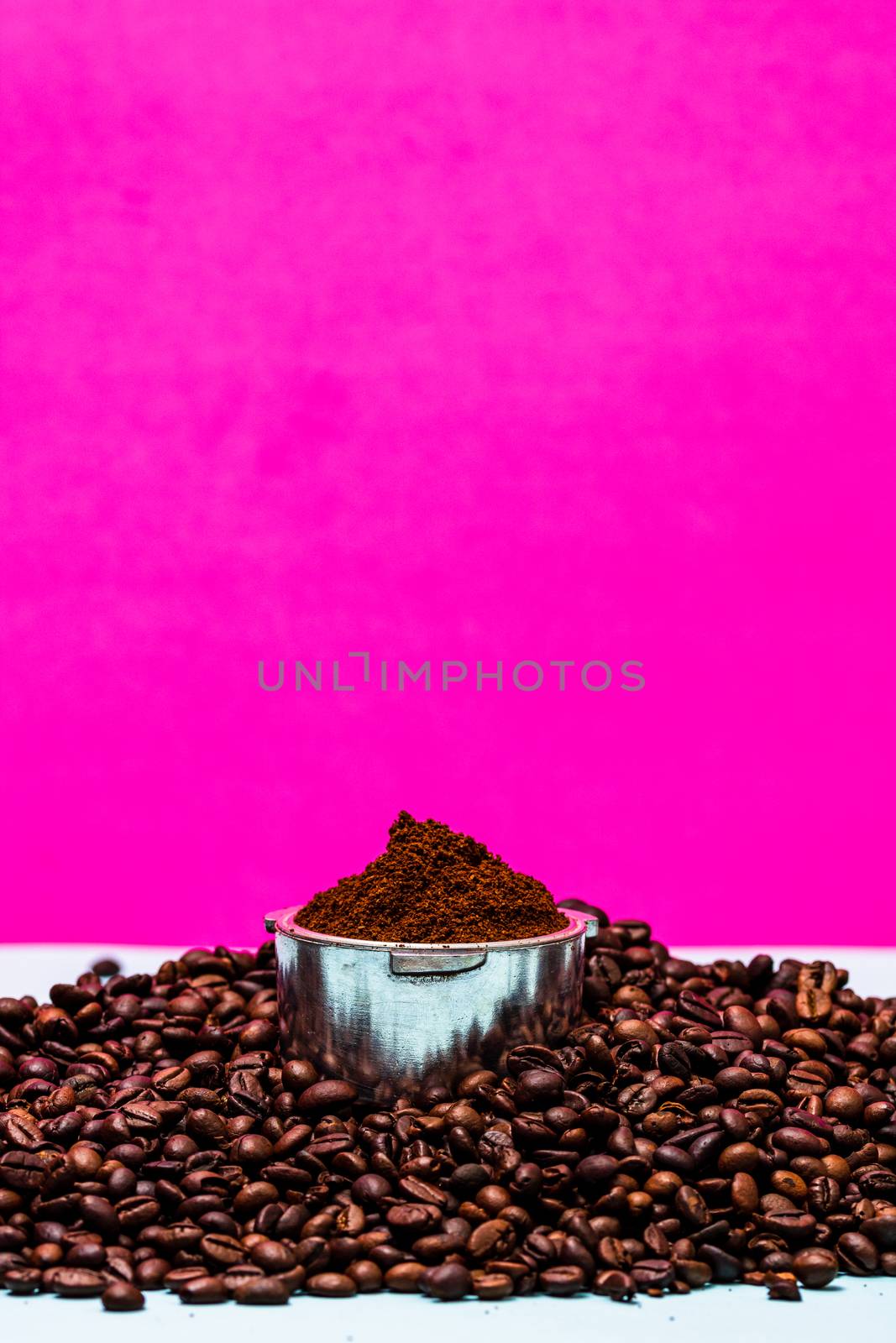 Coffee beans and portafilter with ground coffee in a composition on a pink background.