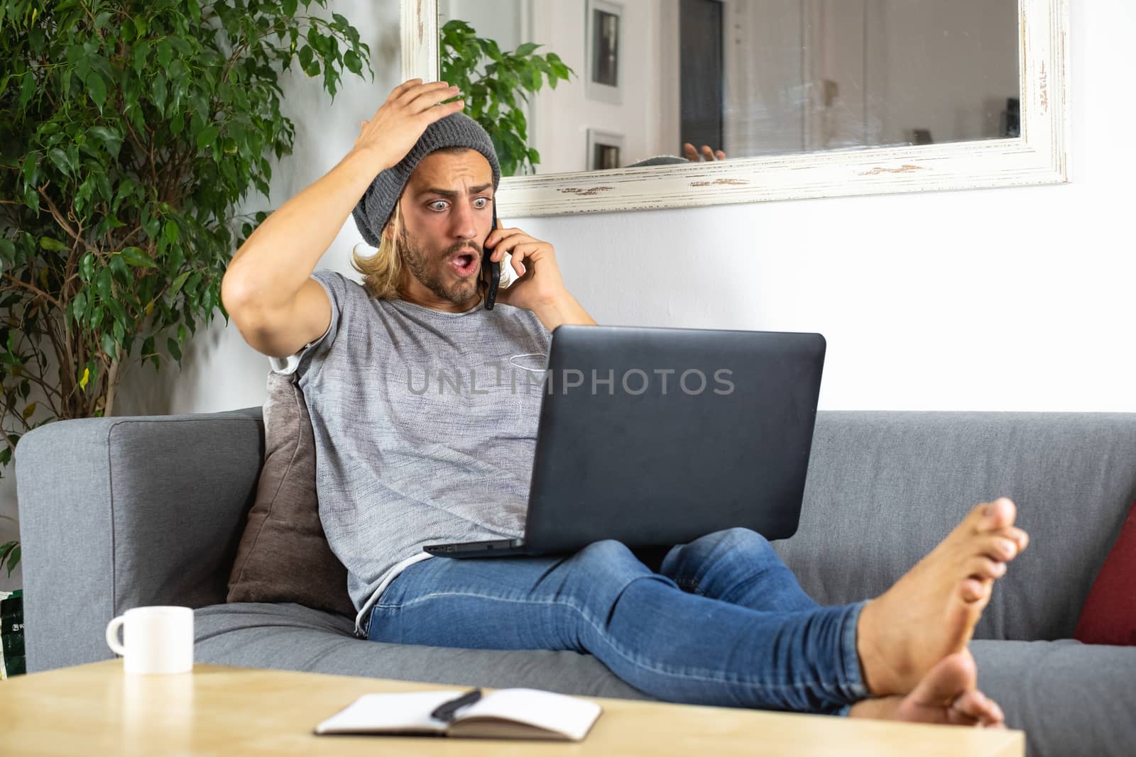 Handsome young business caucasian man working at home using laptop and talking with mobile phone feeling worried