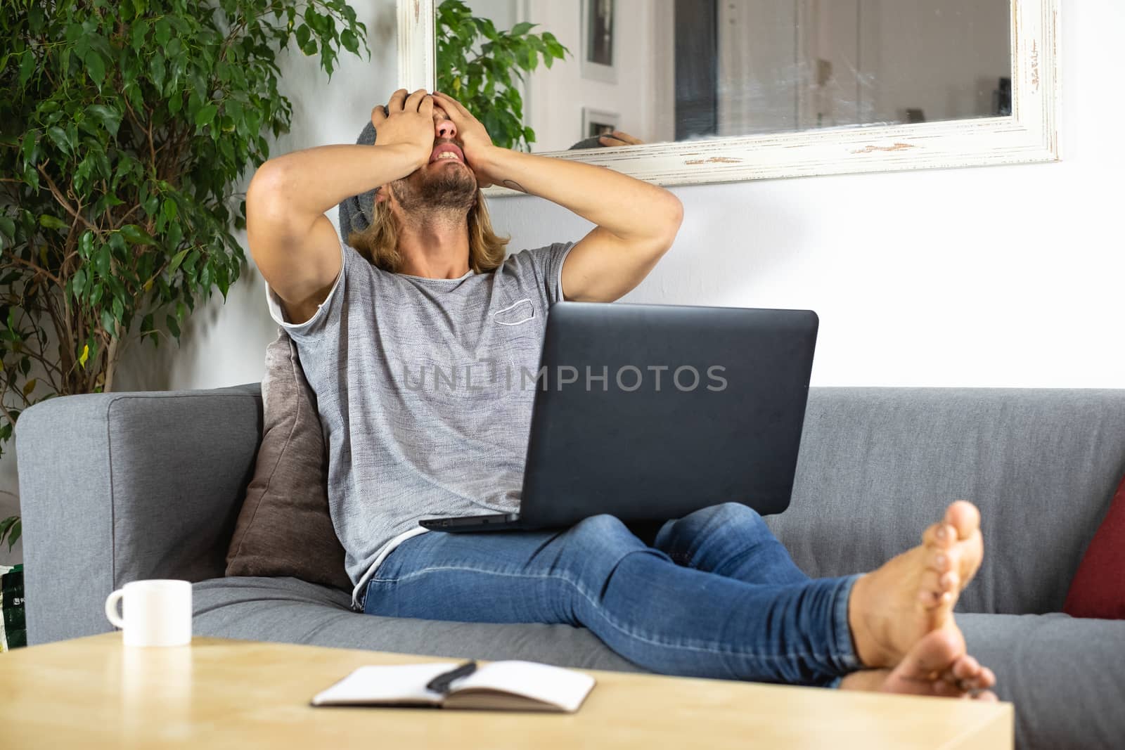 Handsome young business caucasian man working at home using laptop and talking with mobile phone feeling bad